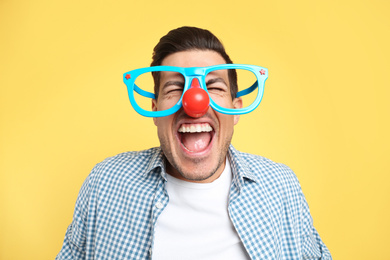 Photo of Joyful man with funny glasses on yellow background. April fool's day