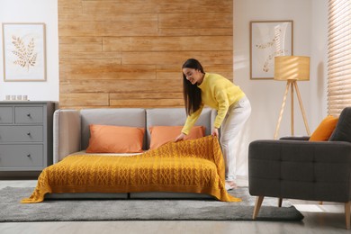 Young woman making bed in room. Modern interior with sleeper sofa