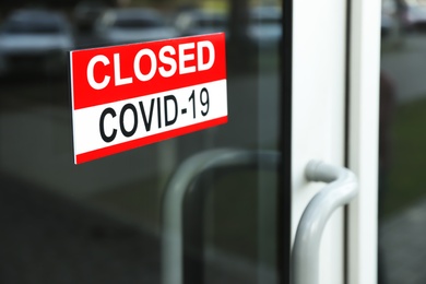 Red sign with words "Closed Covid-19" hanging on glass door