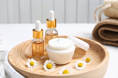 Composition with chamomile flowers and cosmetic products on wooden plate, closeup