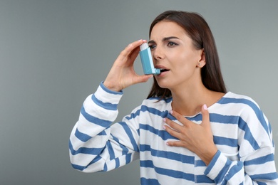 Young woman using asthma inhaler on color background