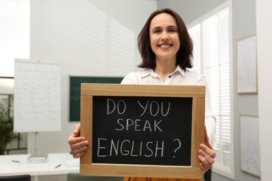Teacher holding small chalkboard with inscription Do You Speak English? in classroom