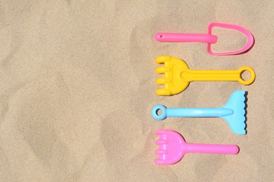 Photo of Bright plastic rakes and shovel on sandy beach, flat lay. Space for text