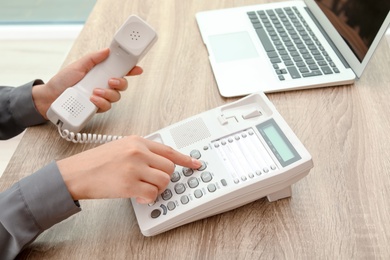 Woman dialing number on telephone at table indoors, closeup