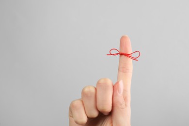 Woman showing index finger with tied red bow as reminder on light grey background, closeup