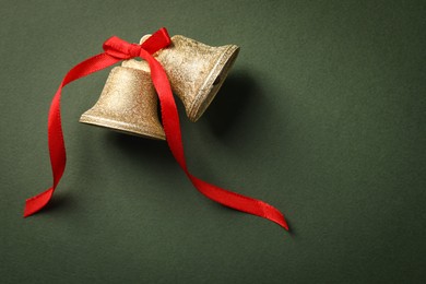 Photo of Bells with red bow on dark green background, flat lay. Space for text. Christmas decor
