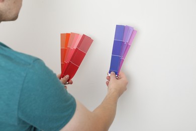 Photo of Man with palette choosing color for painting wall indoors, closeup. Interior design