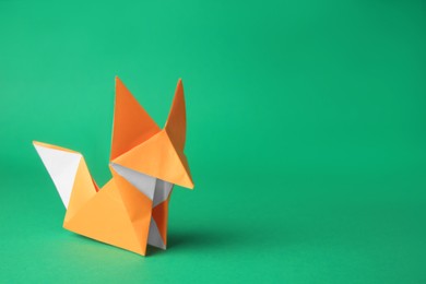 Photo of Origami art. Handmade orange paper fox on green background, space for text