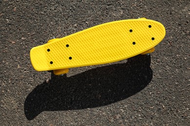 Modern yellow skateboard on asphalt road outdoors, top view