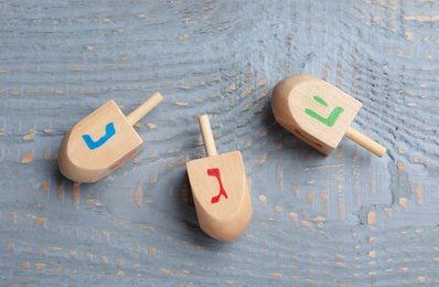 Hanukkah traditional dreidels with letters Nun, He and Gimel on grey wooden table, flat lay