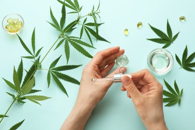 Woman applying CBD oil or THC tincture onto skin at light blue background, top view