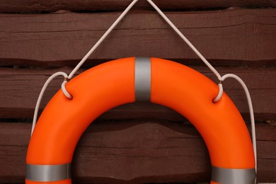 Orange lifebuoy hanging on brown wooden fence, closeup. Rescue equipment
