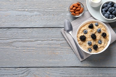 Tasty oatmeal porridge with blackberries and blueberries served on light grey wooden table, flat lay. Space for text