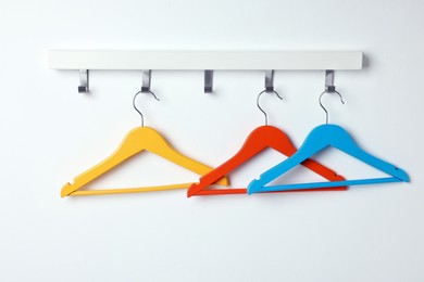 Rack with empty bright clothes hangers on white wall