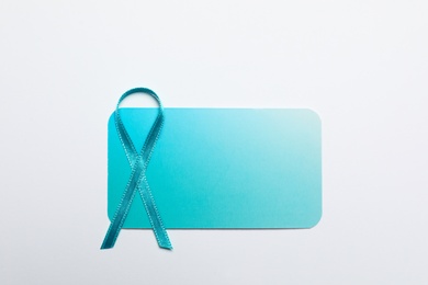 Teal awareness ribbon and card on white background, top view. Symbol of social and medical issues