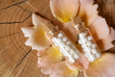 Photo of Bottles of homeopathic remedy and flower petals on wooden background, flat lay