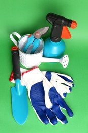 Gardening gloves, tools and watering can on green background