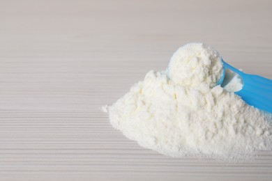 Powdered infant formula and scoop on white wooden table, closeup with space for text. Baby milk