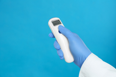 Doctor holding non contact infrared thermometer on light blue background, closeup. Measuring temperature
