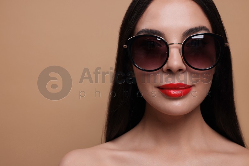 Attractive woman in fashionable sunglasses against beige background, closeup. Space for text