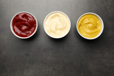 Ketchup, mustard and mayonnaise in bowls on grey table, flat lay. Space for text