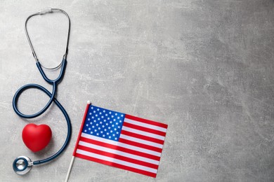 American flag, heart and stethoscope on light grey table, flat lay. Space for text