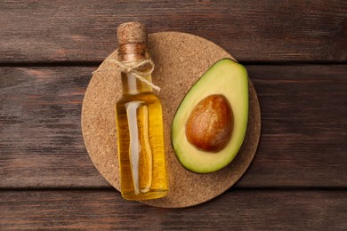 Photo of Glass bottle of cooking oil and cut avocado on wooden table, top view