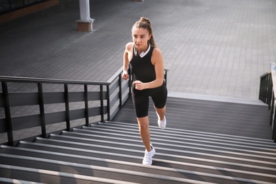 Young woman in sportswear with headphones running up stairs outdoors