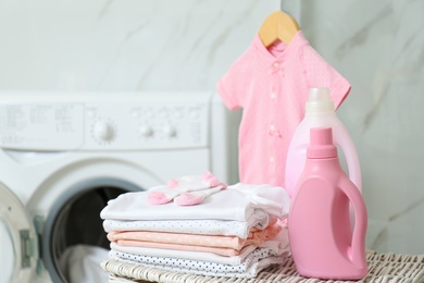 Bottles of detergent and children's clothes on wicker basket in bathroom