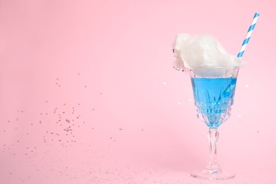 Cocktail with cotton candy in glass on pink background, space for text