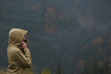 Woman in raincoat enjoying mountain landscape under rain, space for text