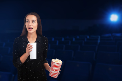 Emotional woman with popcorn and beverage in cinema, space for text