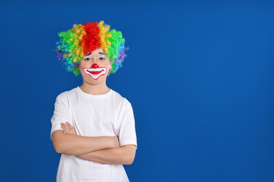 Preteen boy with clown makeup and wig on blue background, space for text. April fool's day