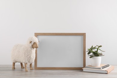 Photo of Blank photo frame, notebooks, houseplant and decorative sheep on wooden table