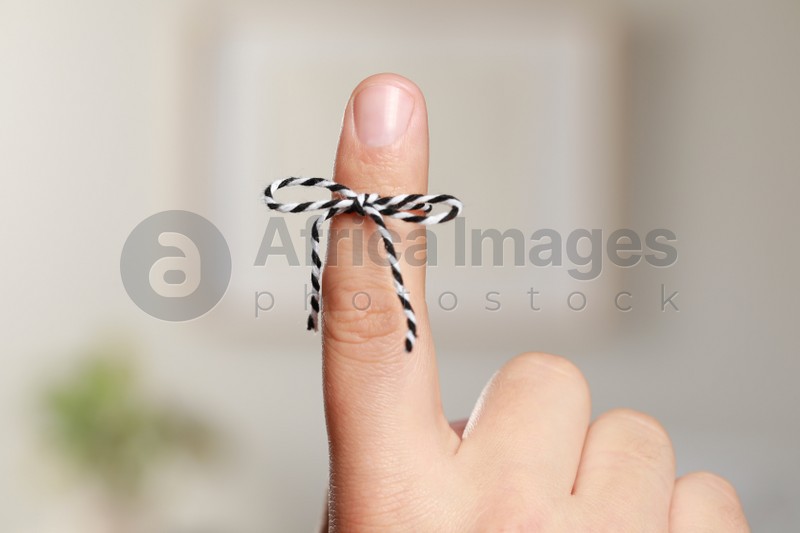 Man showing index finger with tied bow as reminder on blurred background, closeup