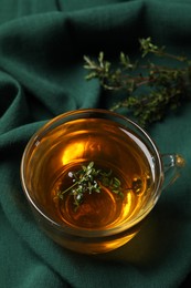 Photo of Glass cup of aromatic herbal tea with thyme on green fabric