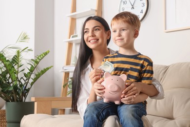 Mother with money and her son holding piggy bank at home, space for text