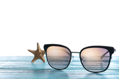 Stylish sunglasses and starfish on light blue wooden table against white background