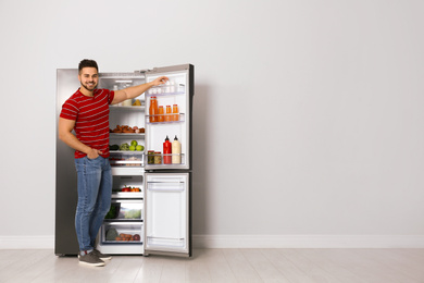 Young man taking yoghurt out of refrigerator indoors, space for text