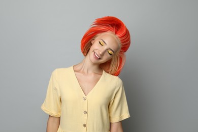 Beautiful young woman with bright dyed hair shaking head on light grey background