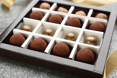 Photo of Different delicious chocolate candies in box on grey table, closeup