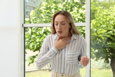 Young woman suffering from pain during breathing near window