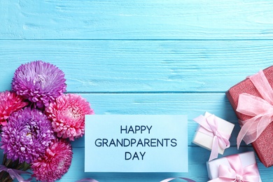 Beautiful flowers, gift boxes and card with phrase Happy Grandparents Day on light blue wooden background, flat lay. Space for text