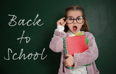 Cute little child wearing glasses near chalkboard with phrase BACK TO SCHOOL