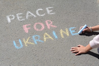 Photo of Girl writing Peace For Ukraine with colorful chalks on asphalt outdoors, closeup