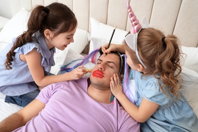 Cute little children painting face of their father while he sleeping in bed at home