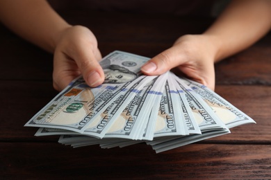 Woman holding dollar banknotes at wooden table, closeup