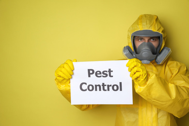 Man wearing protective suit with insecticide sprayer holding sign PEST CONTROL on yellow background