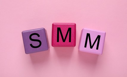 Colorful cubes with abbreviation SMM (Social media marketing) on pink background, flat lay