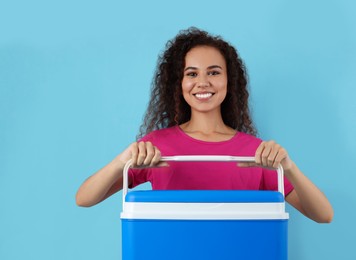Happy young African American woman with cool box on light blue background